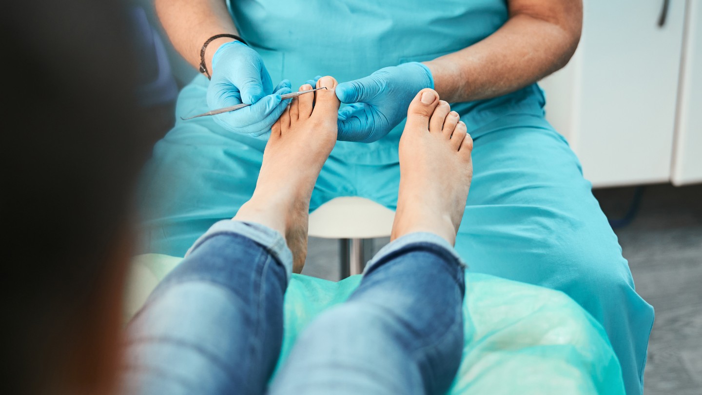 A podiatrist from Hong Kong Foot Clinics examines a patient's bare feet, using a small metal instrument to check the big toe of the left foot.